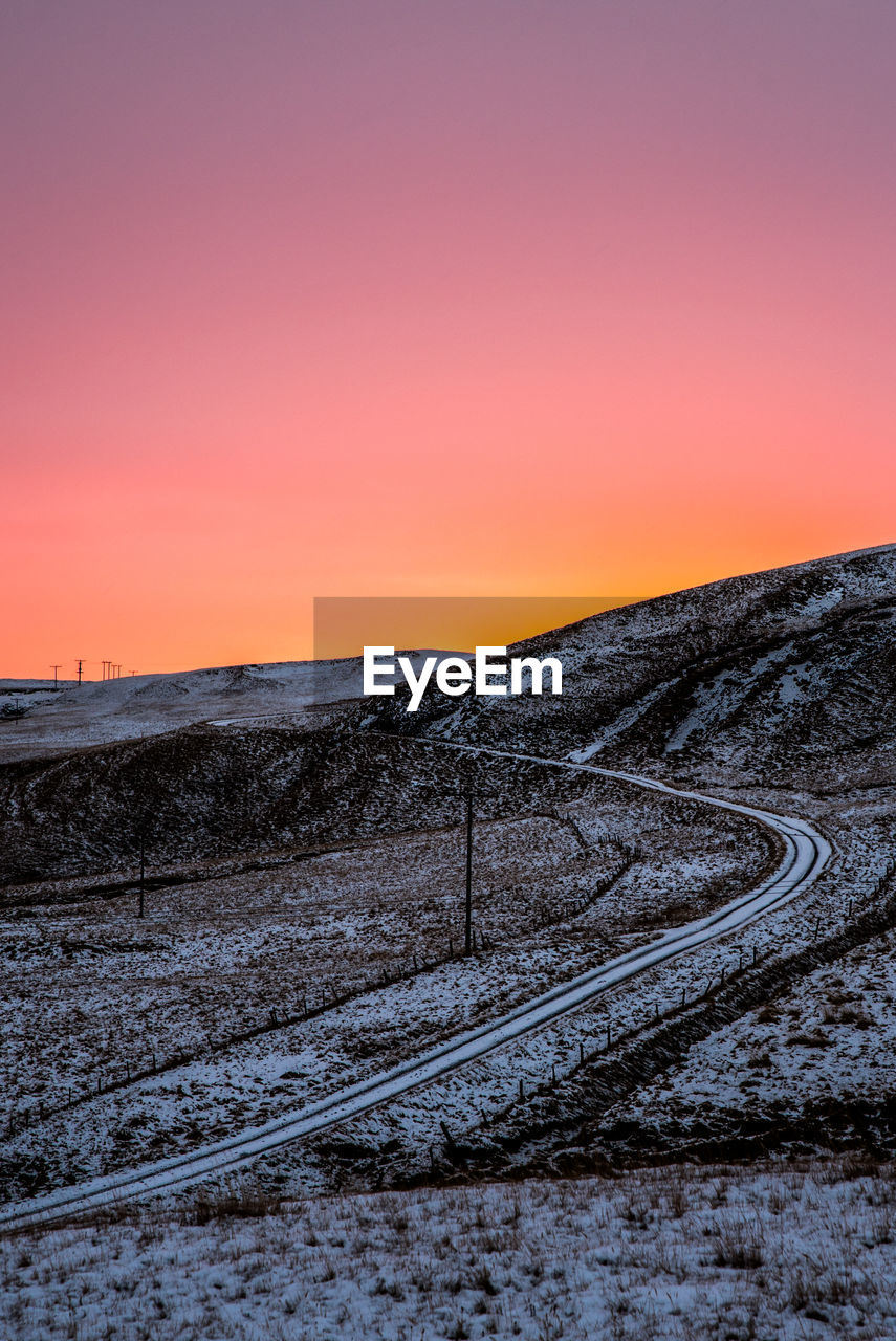 Snow covered road against sky during sunset