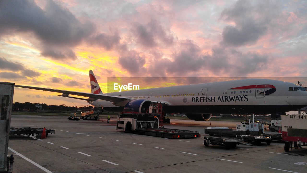 AIRPLANE AT AIRPORT RUNWAY AGAINST SKY DURING SUNSET