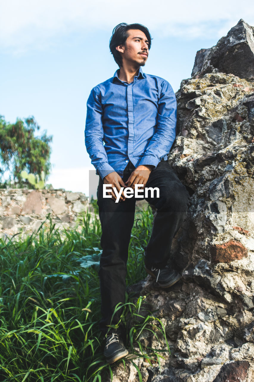 Low angle view of man standing on rock at grassy field against sky