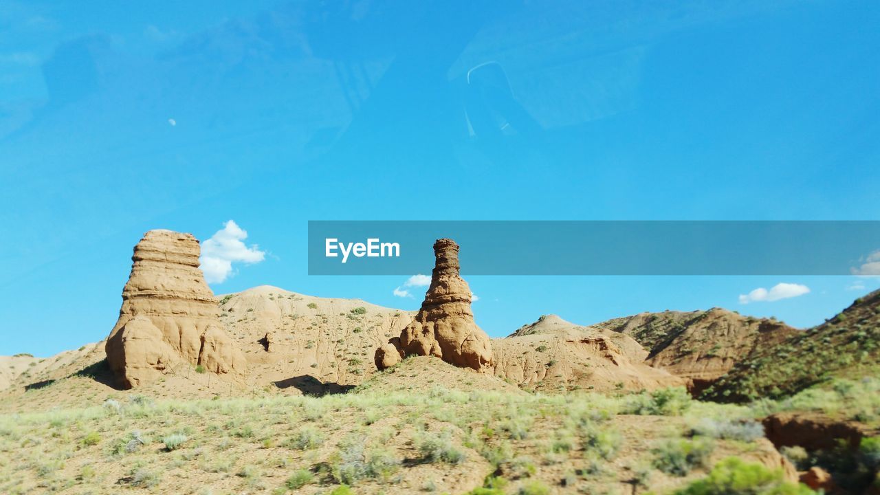 Low angle view of rock formation seen through glass against blue sky