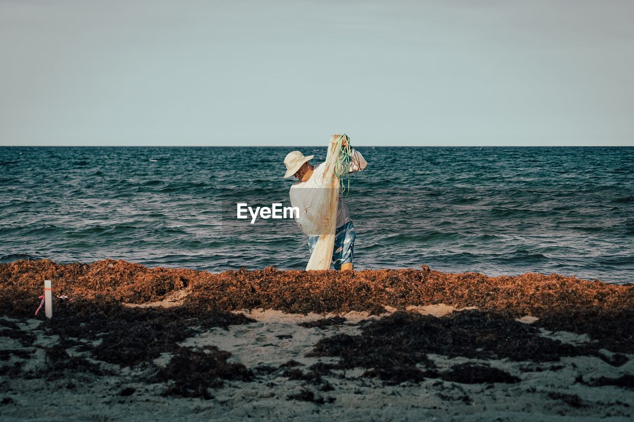Rear view of woman standing at beach against sky