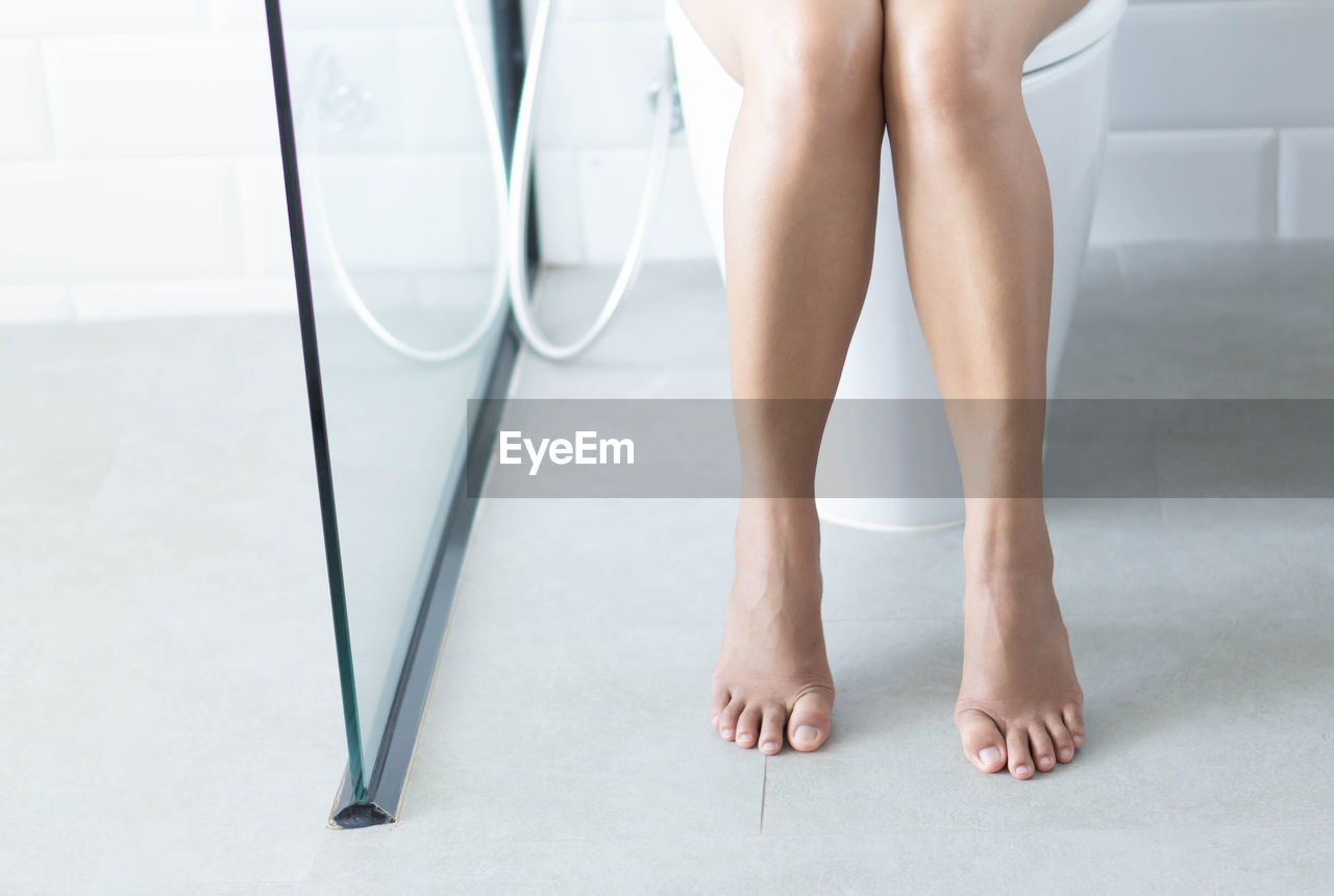 Low section of woman sitting on toilet seat