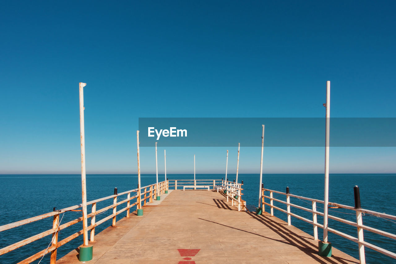 Pier over sea against clear blue sky