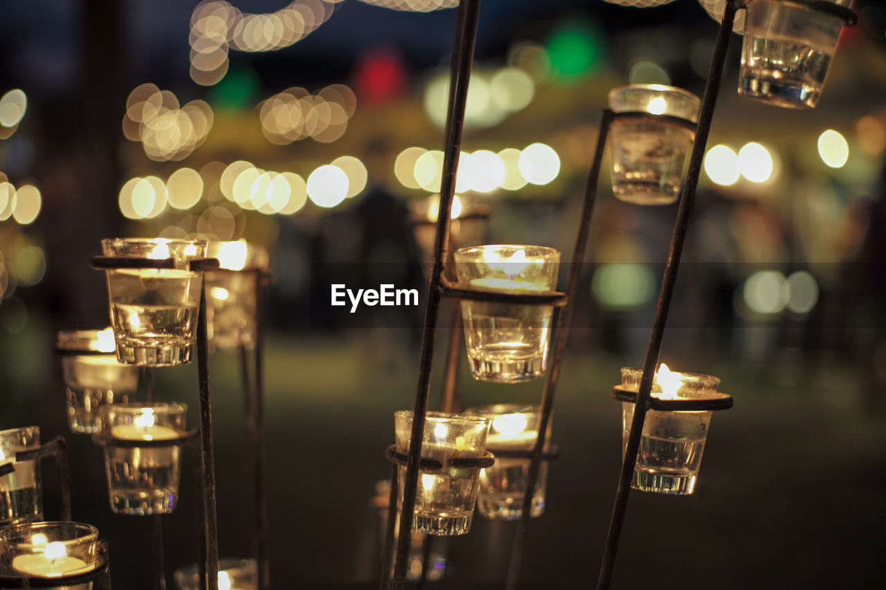 Close-up candle in small glass jars in the steel holder with blurred bokeh lights background