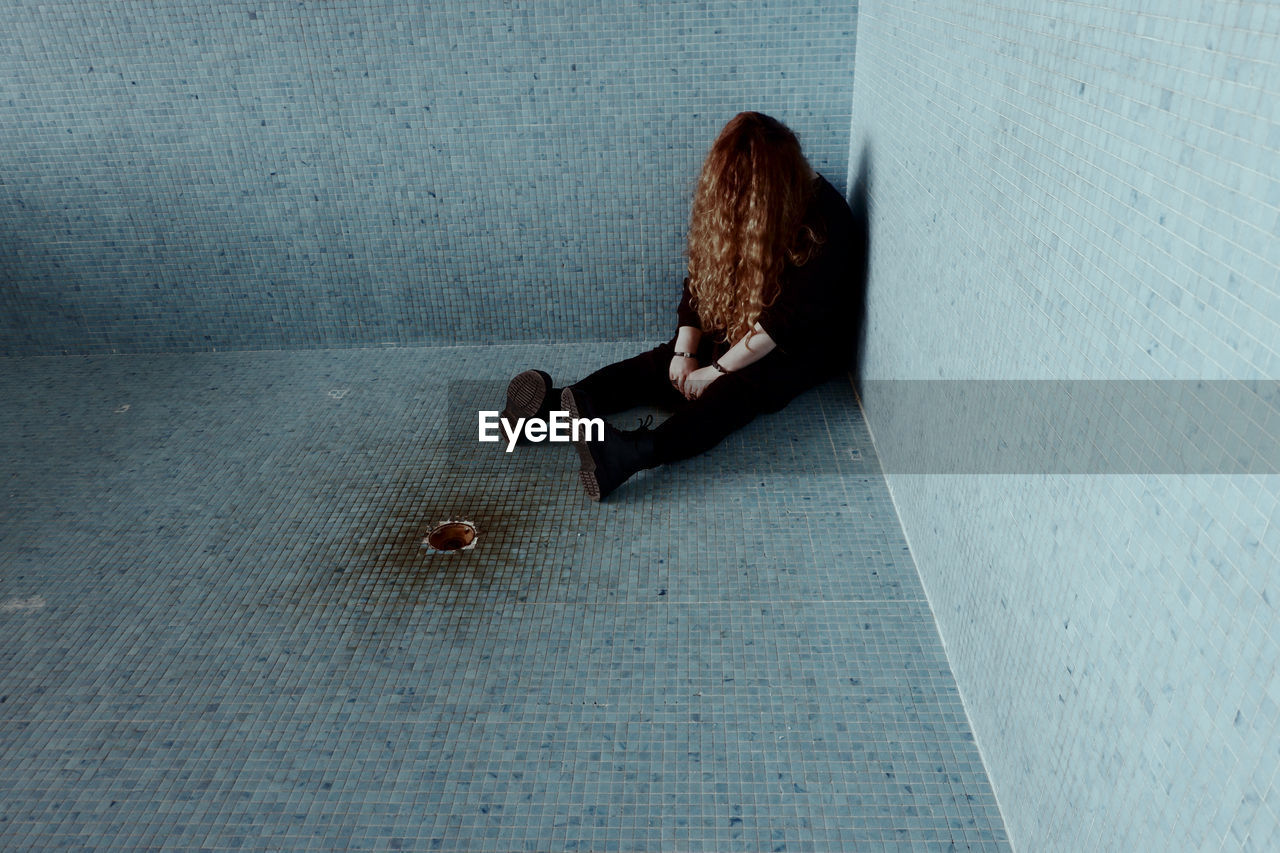 High angle view of sad woman sitting on tiled floor