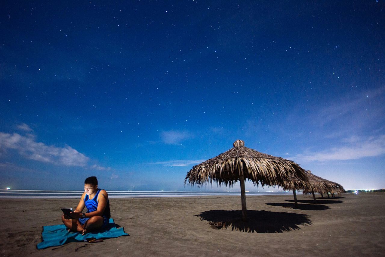 Man sitting on beach against sky at dawn