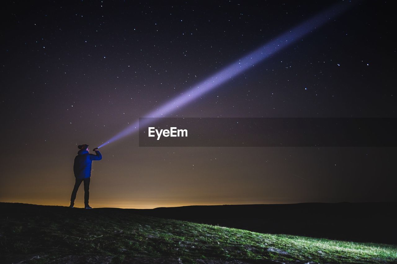 Man pointing flashlight on star field while standing on mountain