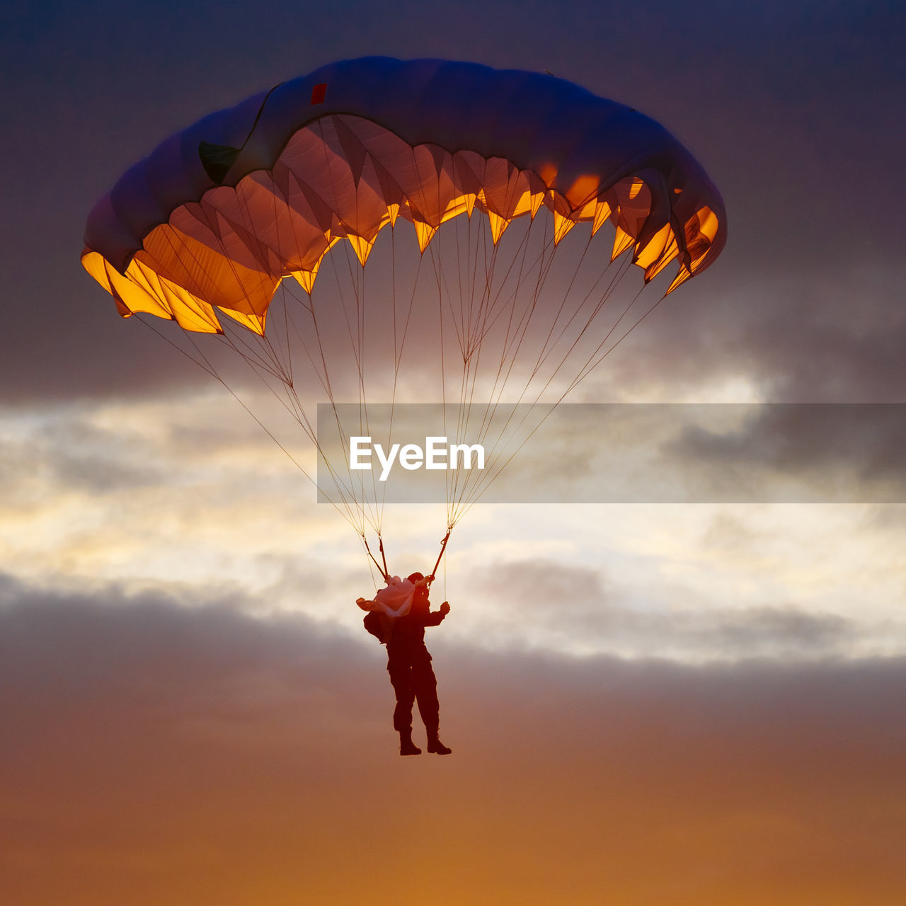 Low angle view of man paragliding against sky during sunset