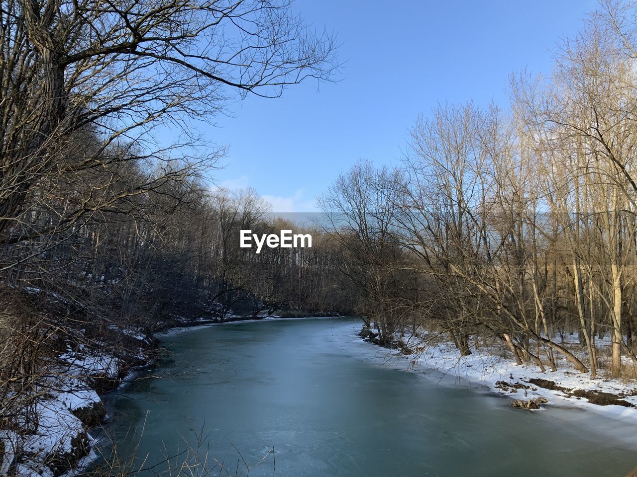 RIVER AMIDST BARE TREES AGAINST SKY DURING WINTER