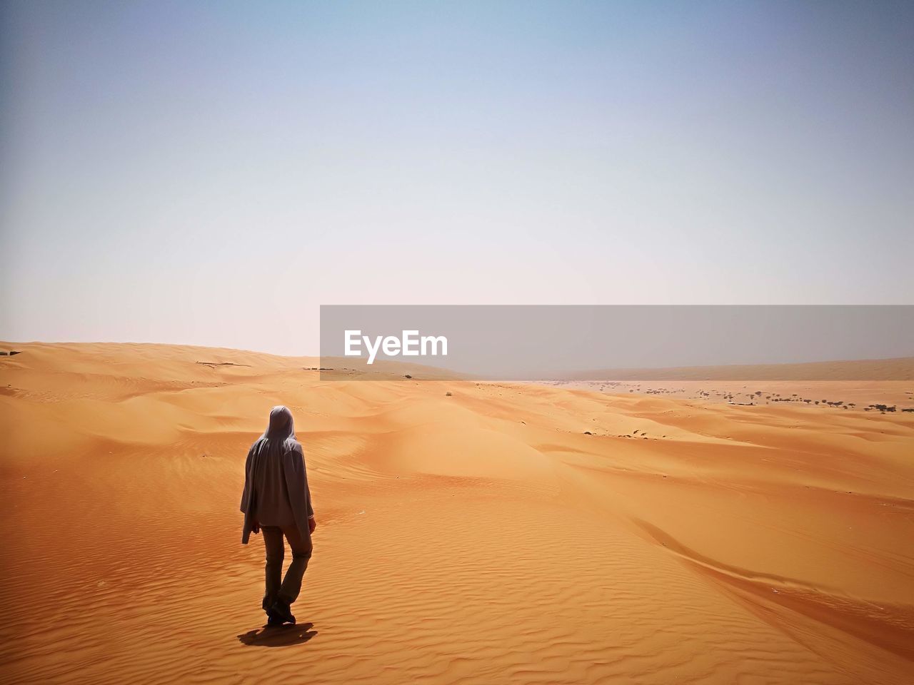 Full length rear view of man walking in desert against clear sky