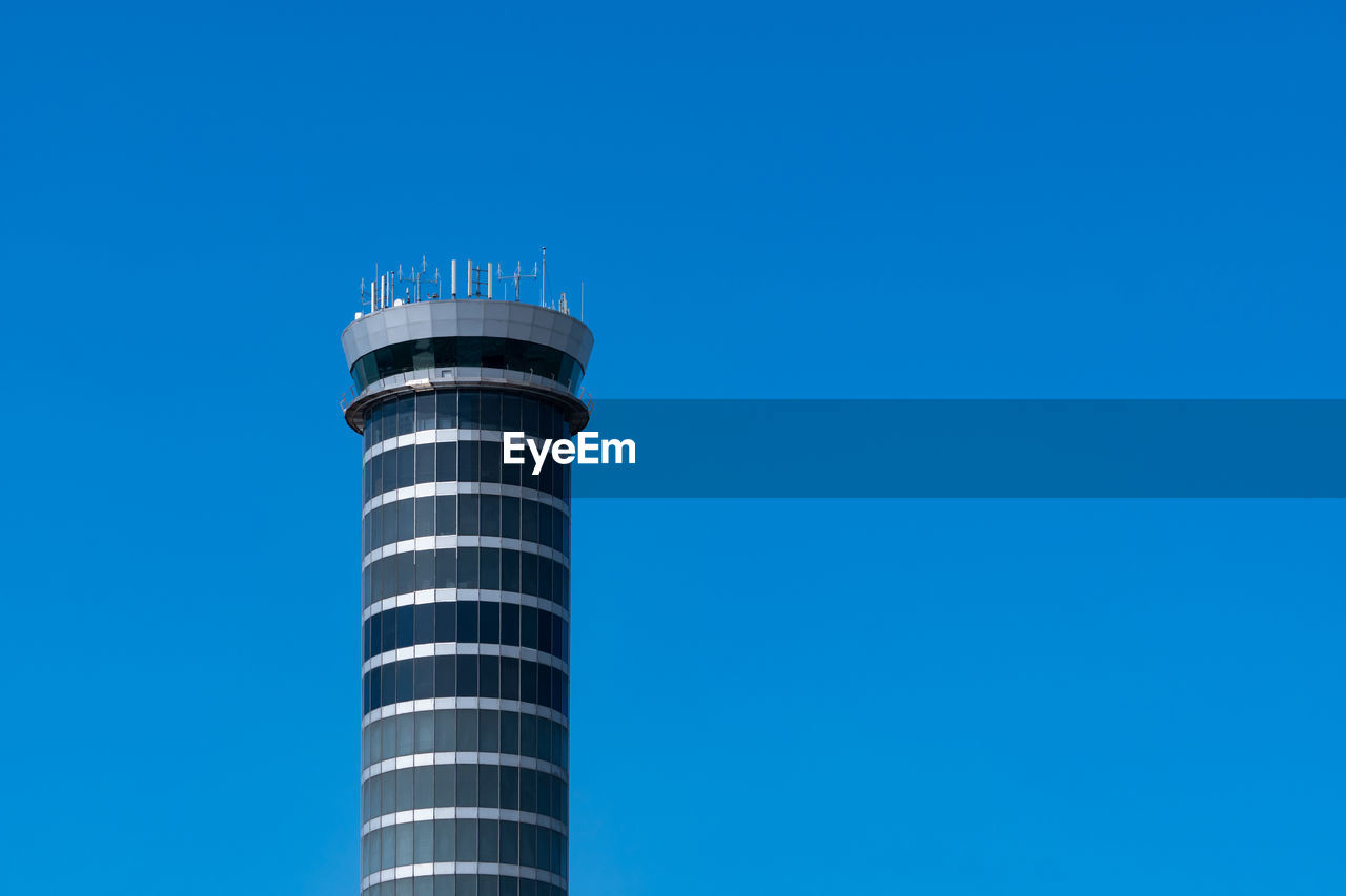 Air traffic control tower in the airport with international flight plane flying on clear blue sky. 