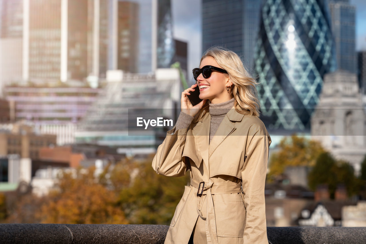 Young woman wearing long coat talking on phone while standing outdoors