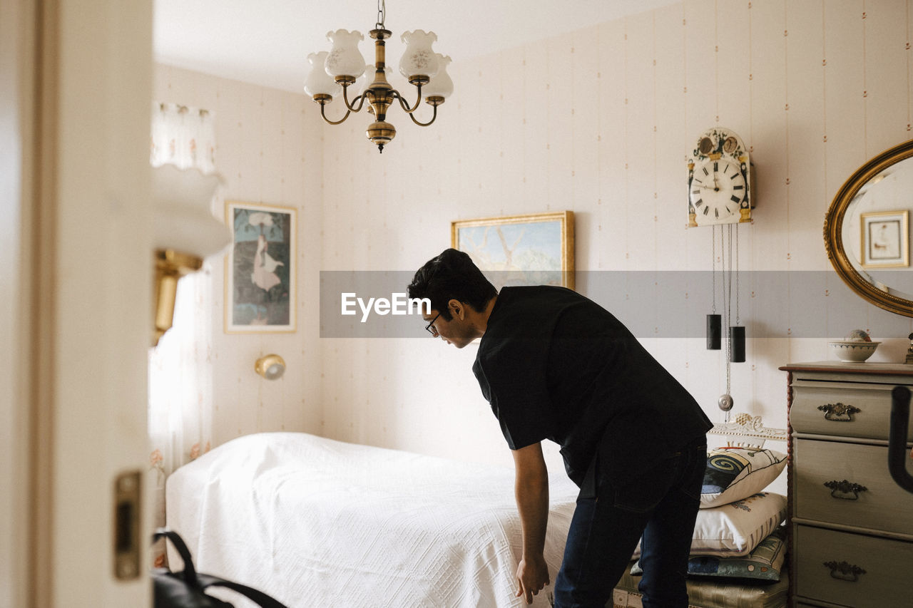 Young male nurse arranging blanket on bed in bedroom