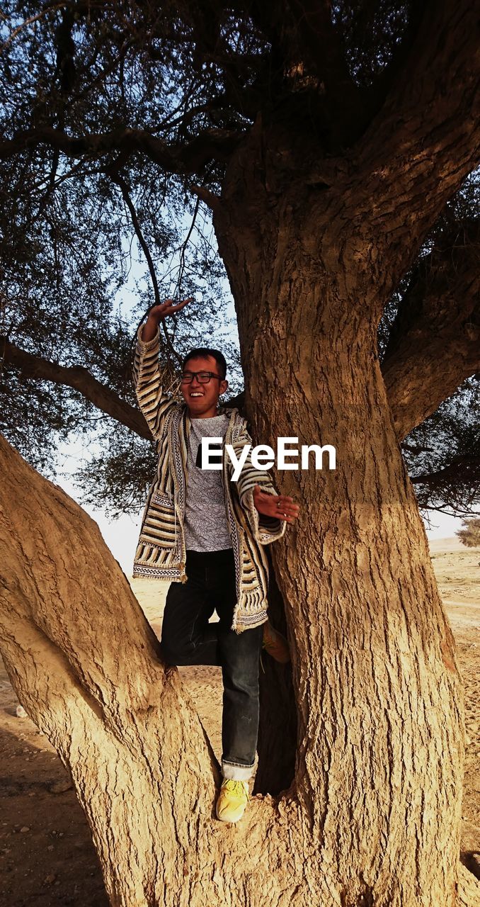 Cheerful man standing on tree branch in forest