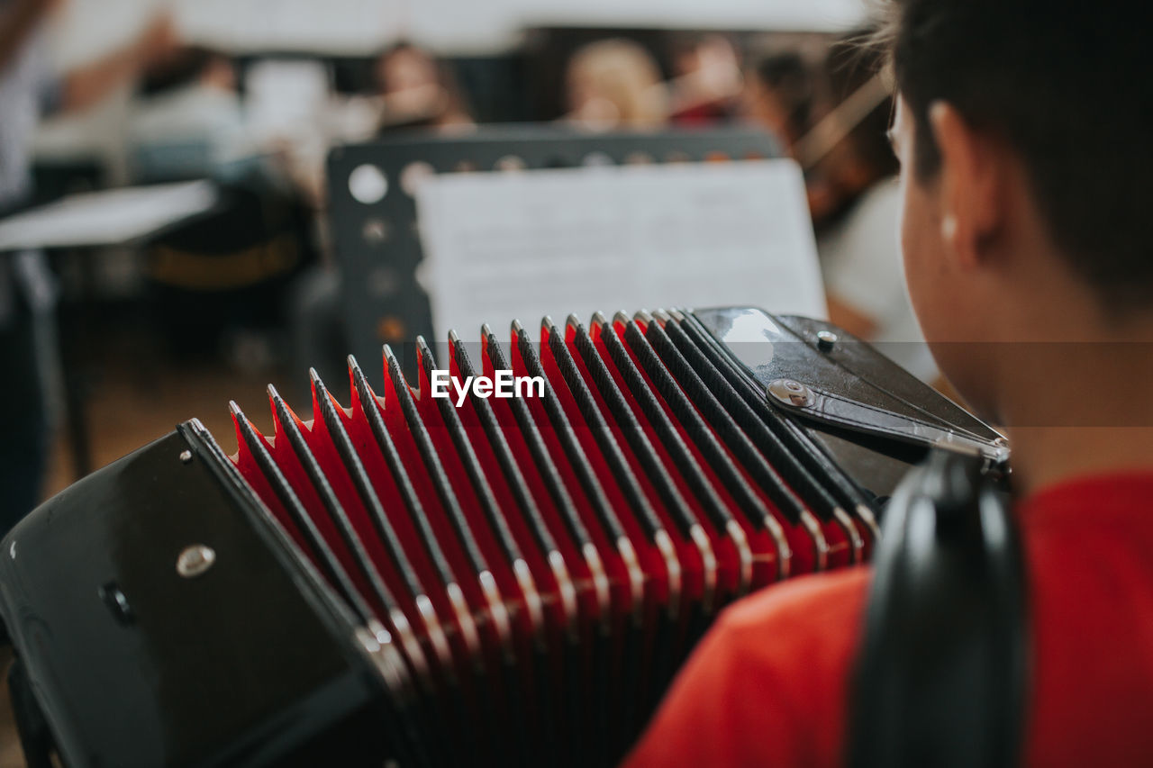 Rear view of man playing accordion in music school