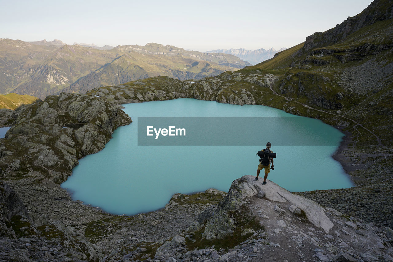 MAN STANDING ON ROCKS AGAINST MOUNTAIN