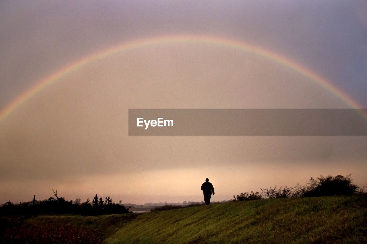 SILHOUETTE PERSON STANDING ON FIELD AGAINST RAINBOW