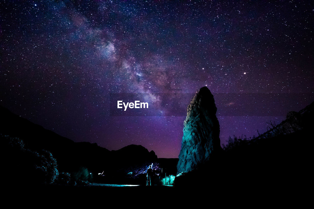 SILHOUETTE PEOPLE ON MOUNTAIN AGAINST STAR FIELD AT NIGHT