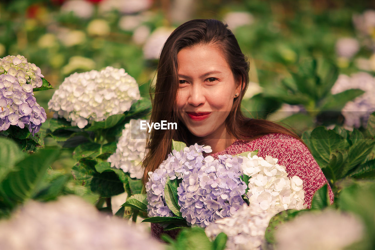 PORTRAIT OF SMILING WOMAN WITH PINK FLOWER