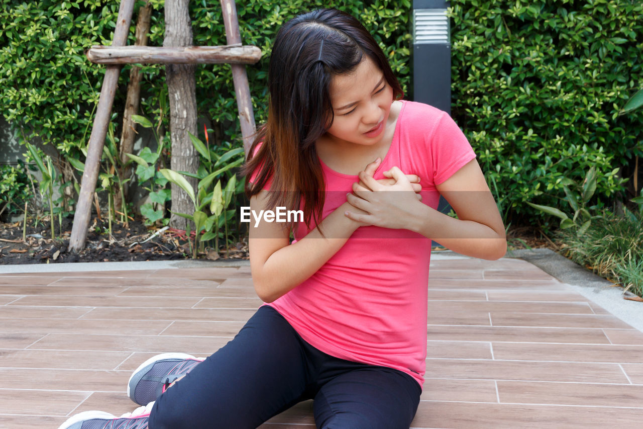 Woman with chest pain sitting on footpath against plants