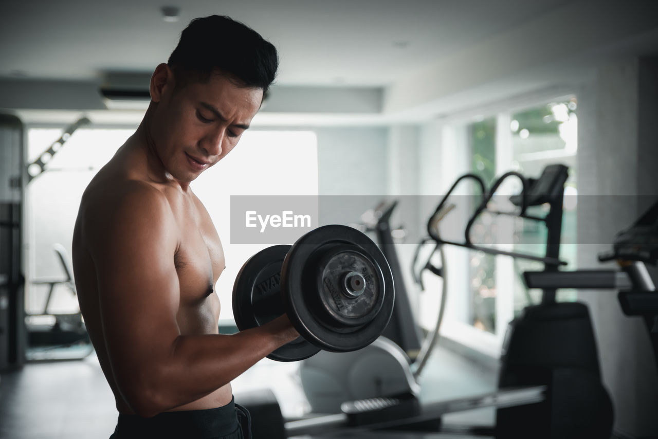 MIDSECTION OF SHIRTLESS MAN STANDING AGAINST WALL