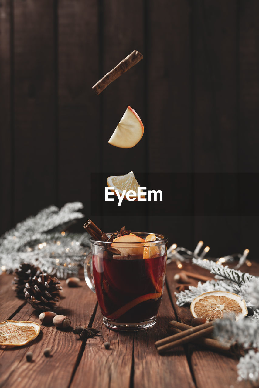 Christmas glass cup or mug with mulled wine on wooden table and background with levitating cinnamon