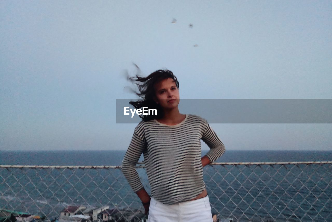 Thoughtful woman standing by sea against sky during sunset