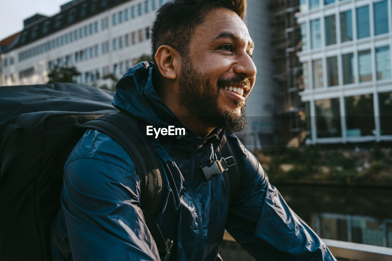 Smiling food delivery person with backpack in city