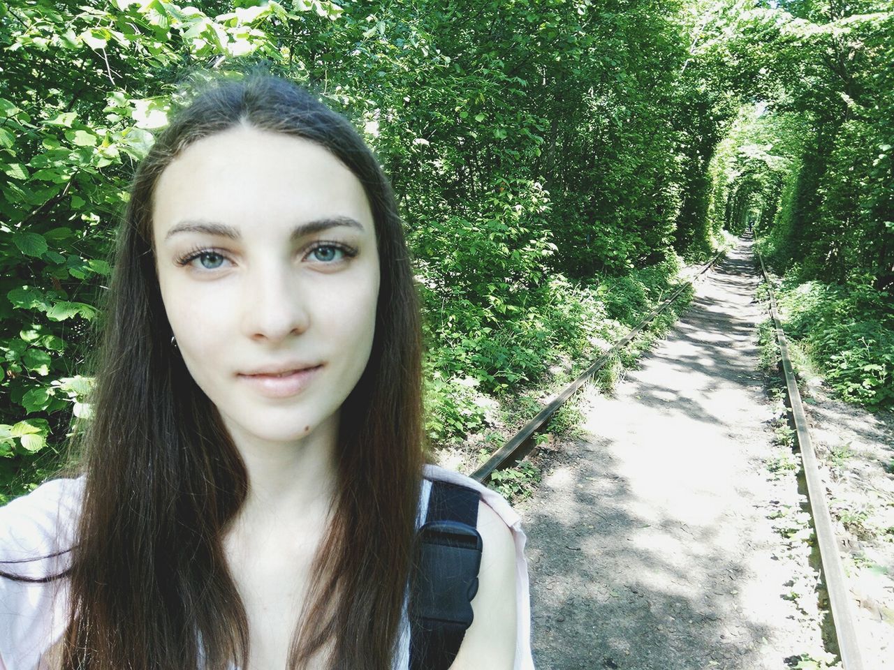 Portrait of young woman with long hair standing by railroad track in forest