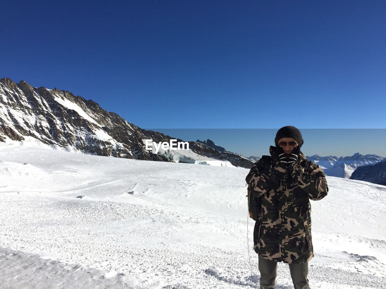 Man wearing warm clothing standing on snow against sky during sunny day