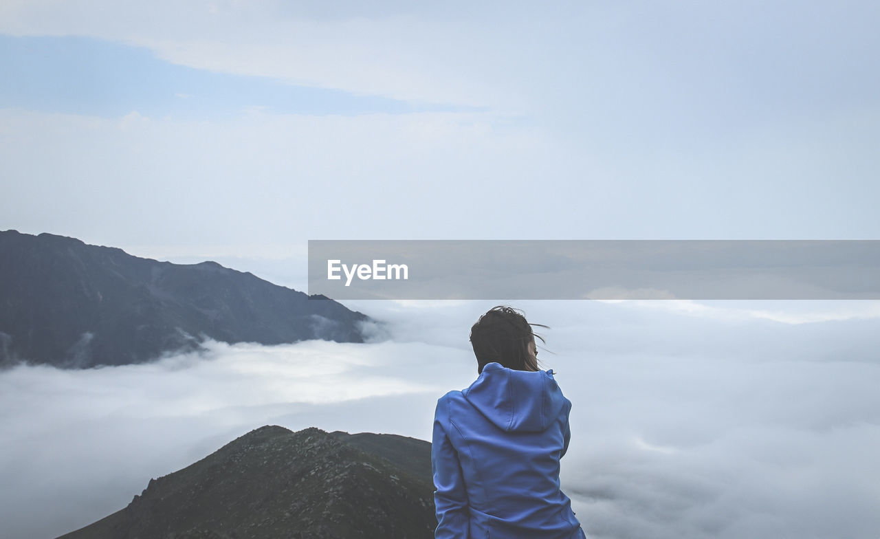 Rear view of woman looking at cloudscape while sitting on mountain