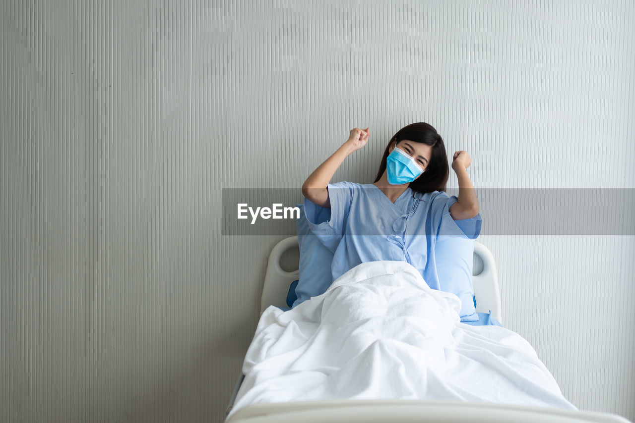 Portrait of young woman sitting on bed against white wall