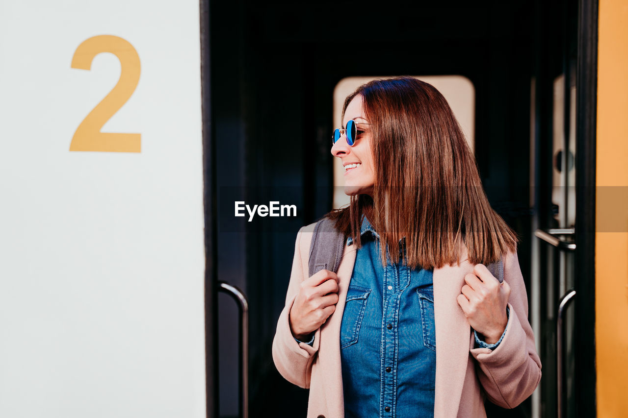 Smiling young backpacker caucasian woman standing on wagon at train station. travel concept