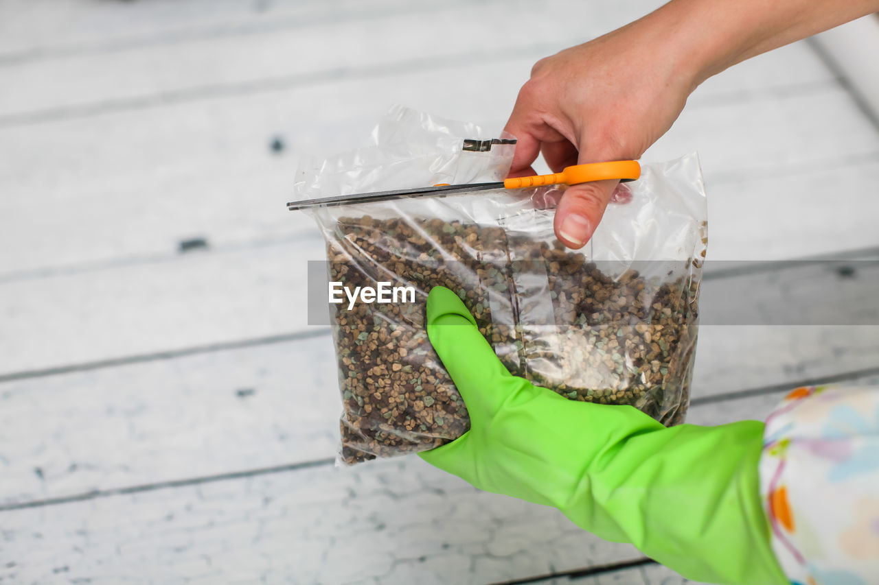 Cropped hands of person cutting bag with stones on table