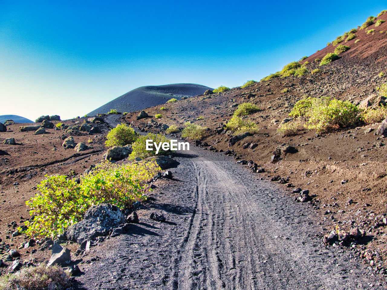 Scenic view of road amidst mountains against clear blue sky