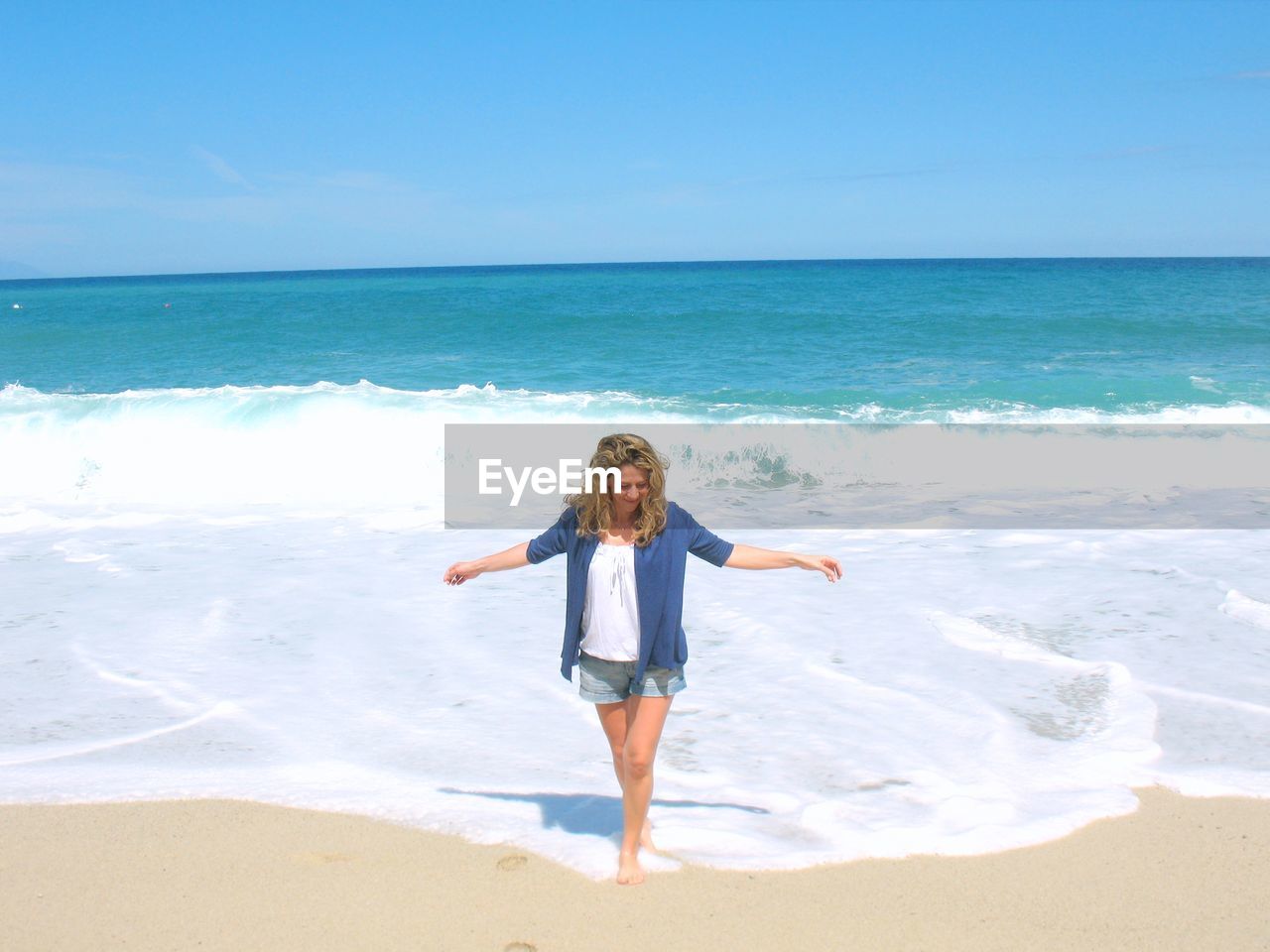 Full length of young woman standing with arms outstretched at beach