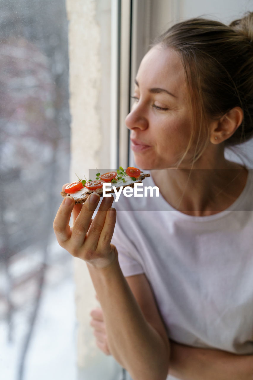 Close-up of woman eating food while looking out of window