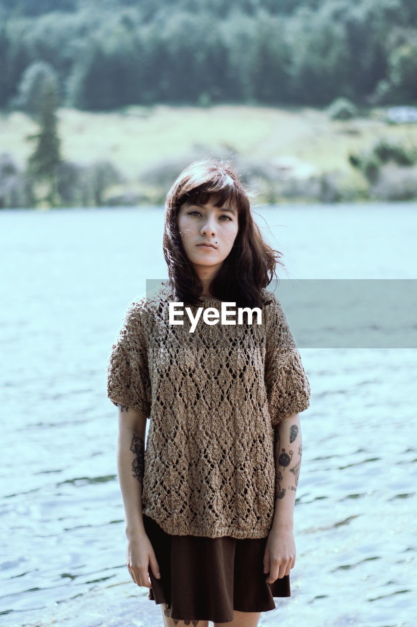 PORTRAIT OF YOUNG WOMAN STANDING AGAINST WATER