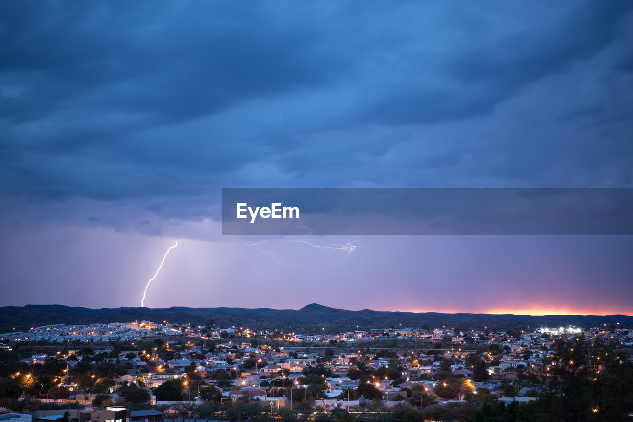 Aerial view of illuminated cityscape against cloudy sky during storm