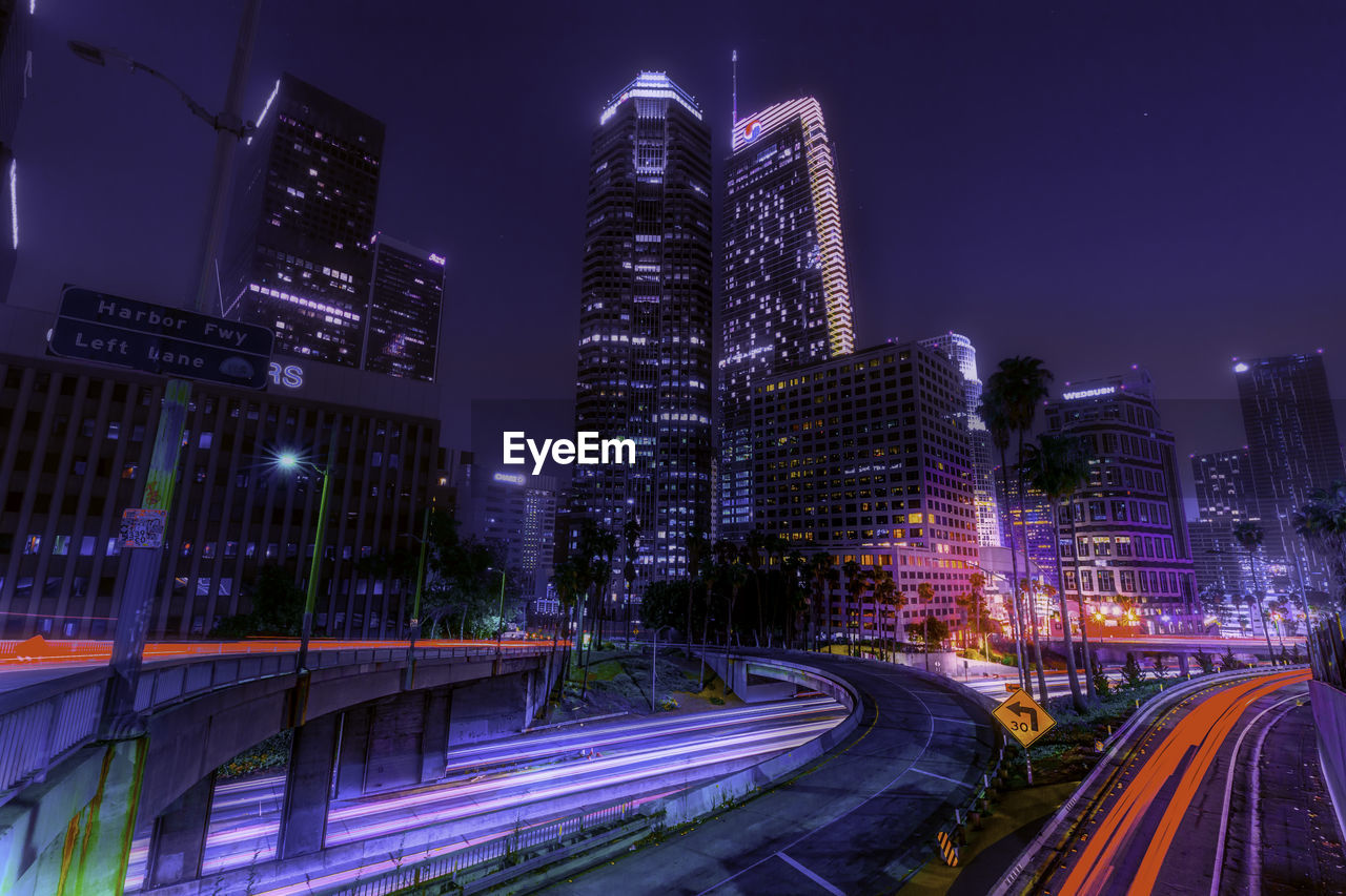 Light trails on street and buildings in city against sky at night