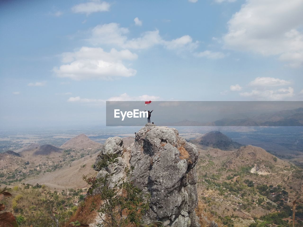 MAN STANDING ON ROCK WITH MOUNTAIN AGAINST SKY