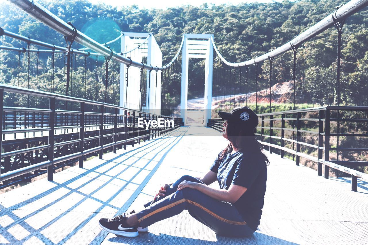 SIDE VIEW OF MAN SITTING ON BRIDGE AGAINST CLEAR SKY