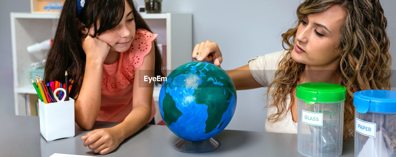 Female teacher giving ecology lesson with handmade globe world to girl student