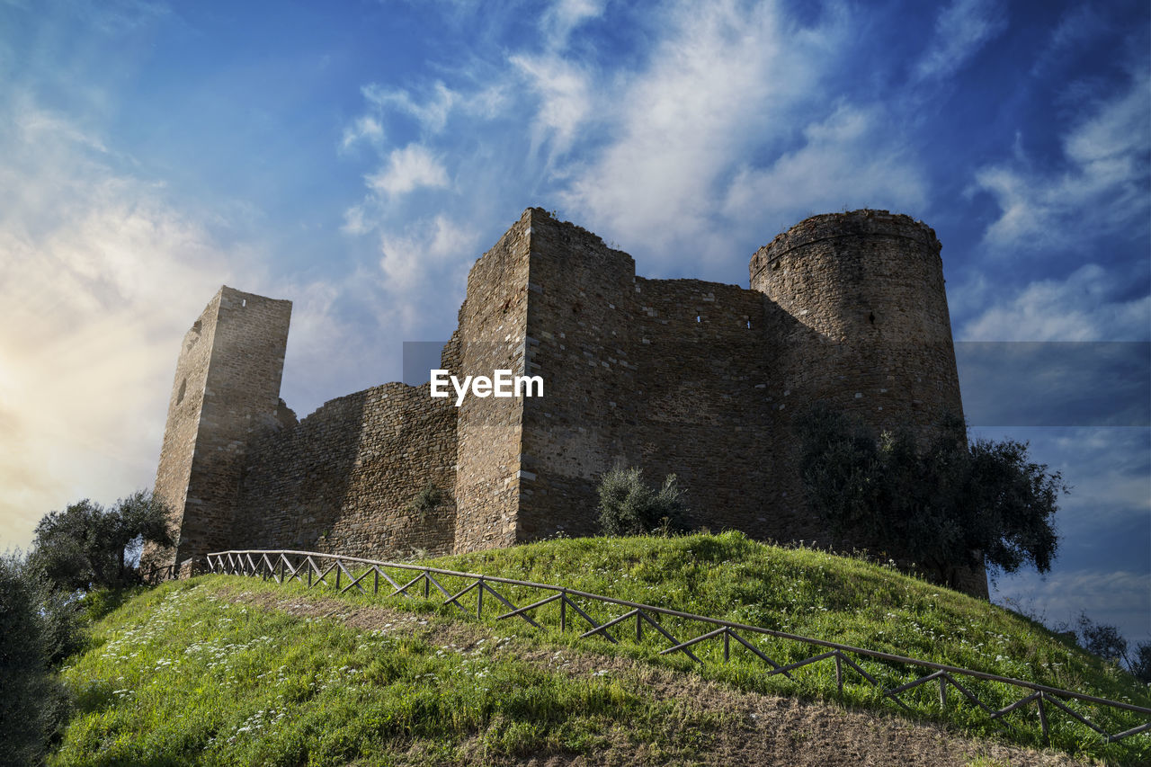 sky, architecture, history, the past, castle, cloud, building, built structure, ruins, plant, nature, ancient, travel destinations, building exterior, château, old ruin, travel, no people, old, fortification, hill, rock, tree, outdoors, fort, low angle view, rural area, tourism, landmark, medieval, wall, day, land, blue, grass