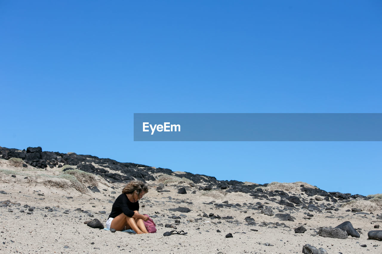 Woman sitting on rock against clear sky