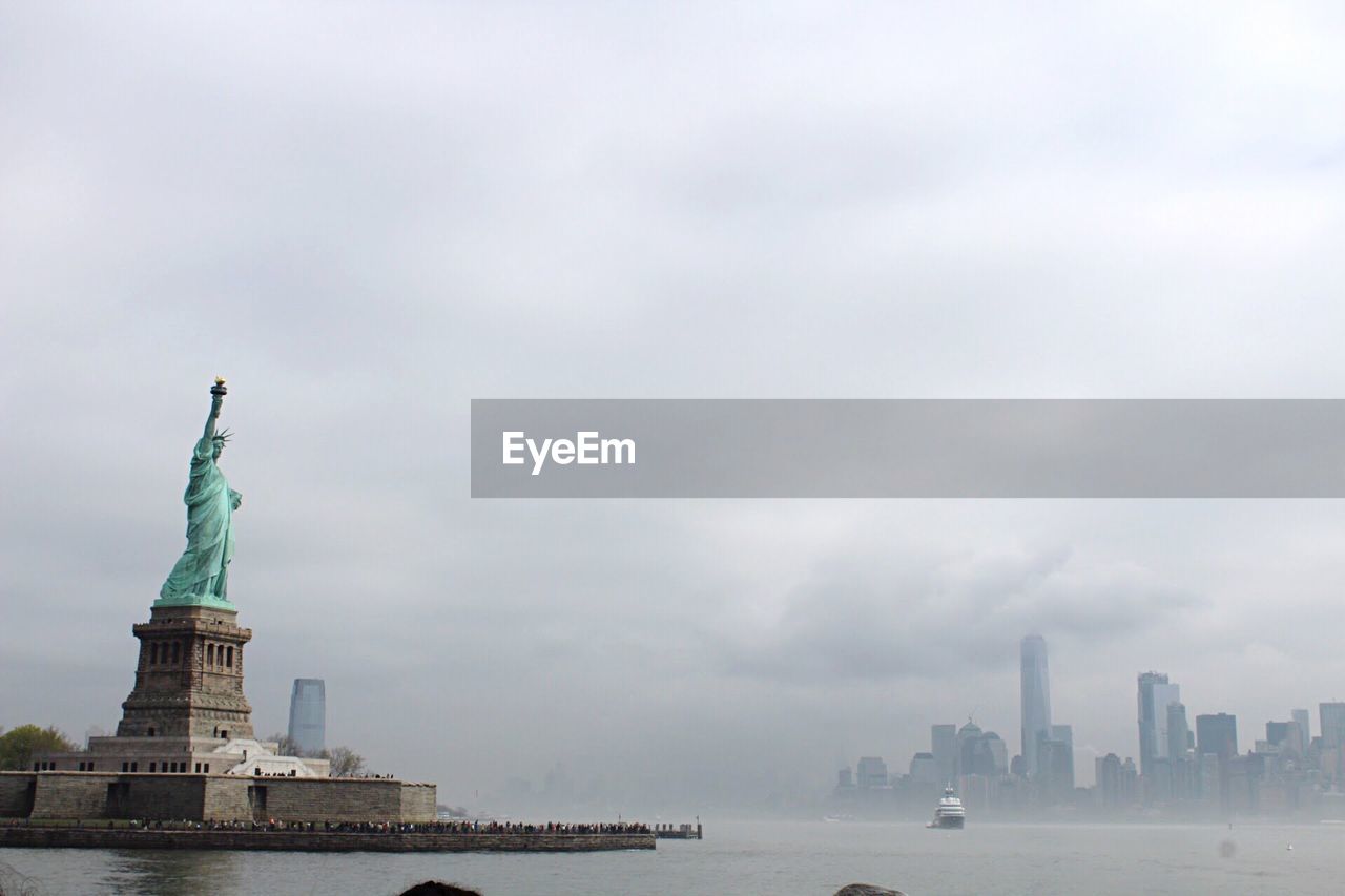 Statue of liberty by hudson river against cloudy sky