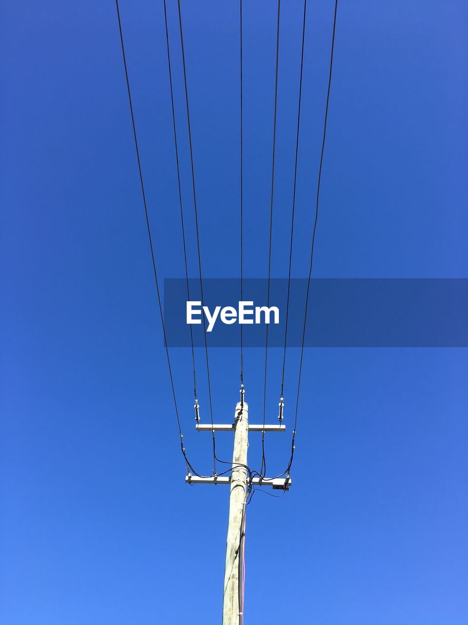 Low angle view of telephone pole against clear blue sky