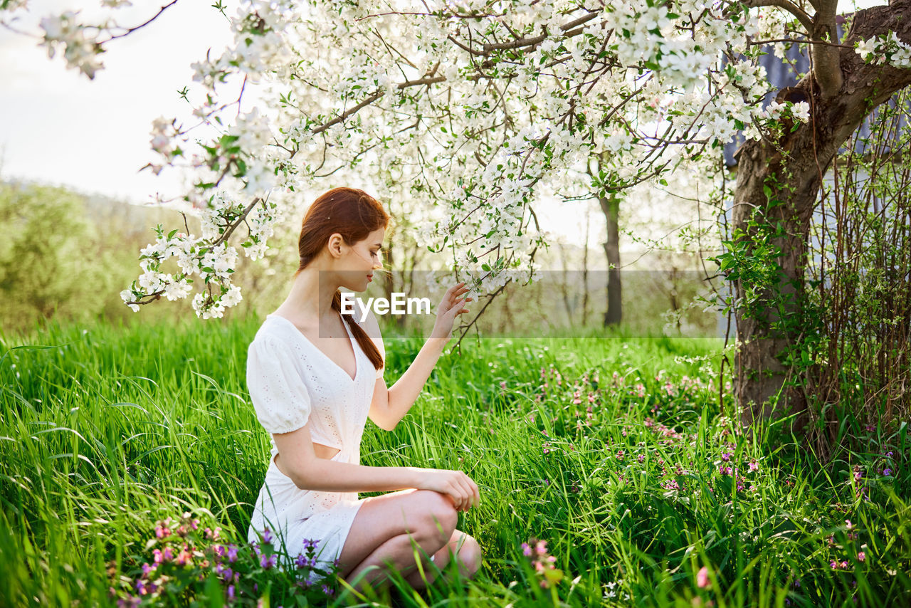 side view of young woman sitting on grassy field