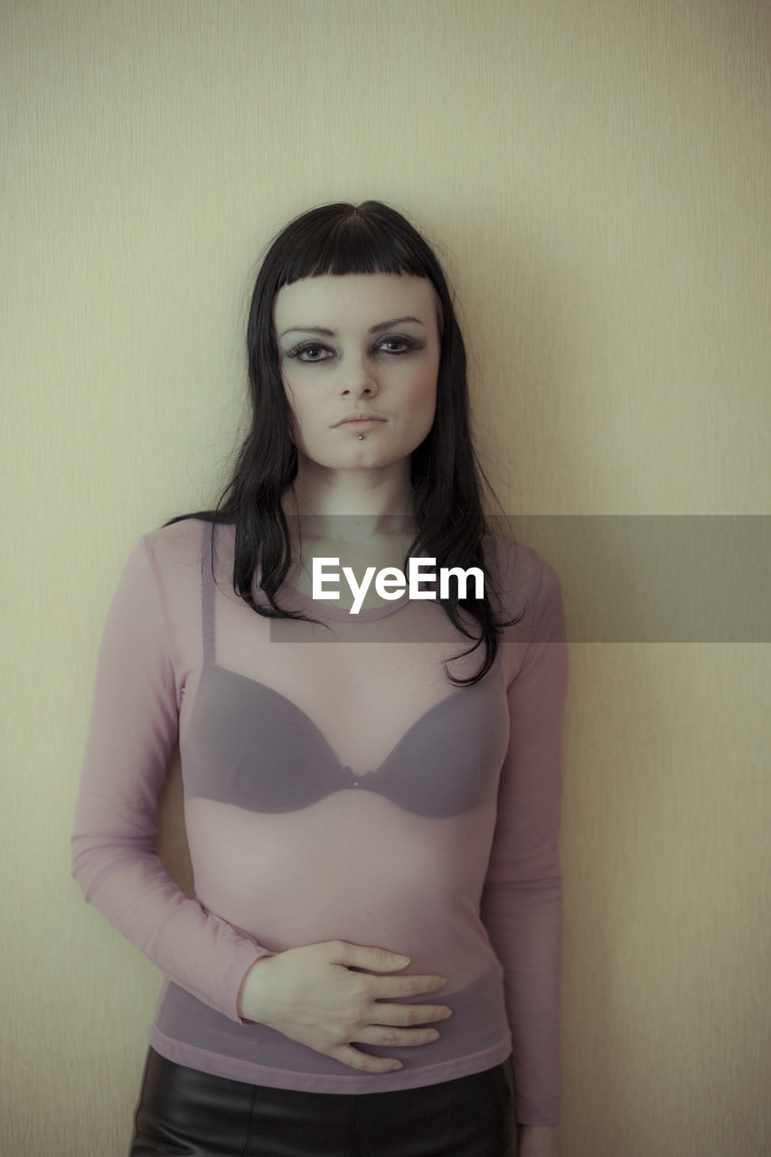 one person, portrait, women, young adult, looking at camera, adult, hairstyle, long hair, indoors, front view, standing, brown hair, studio shot, three quarter length, female, clothing, fashion, photo shoot, person, wall - building feature, white, serious, waist up, pink, human hair, individuality, casual clothing, skin