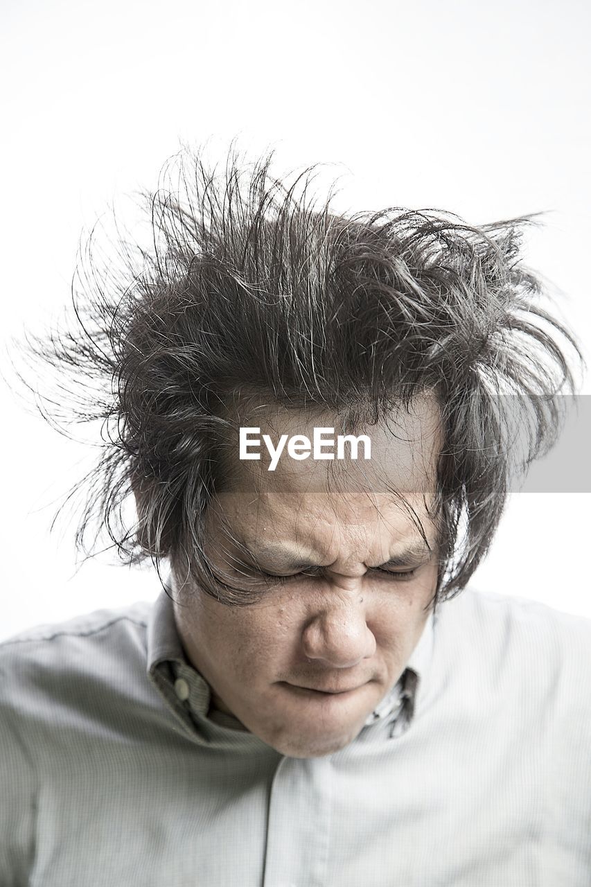 Close-up of frustrated man tossing hair against white background